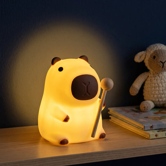 Veilleuse capybara en silicone Halume sur une étagère, à côté d'un mouton en crochet et de livres