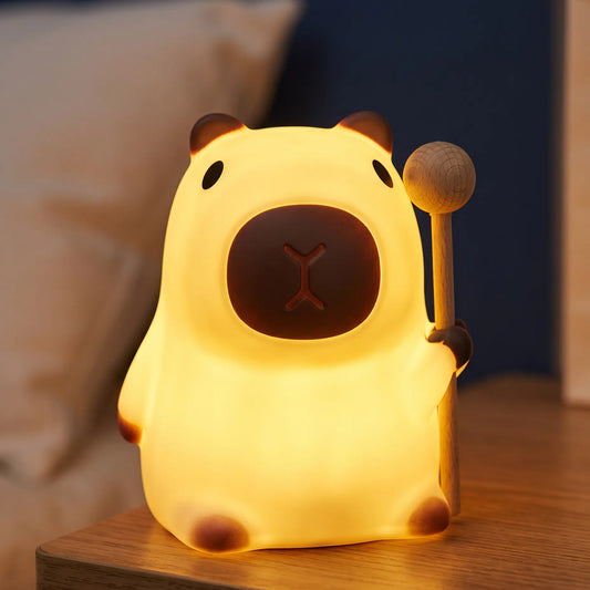 Veilleuse capybara en silicone Halume allumée sur une table de chevet, avec son maillet en bois